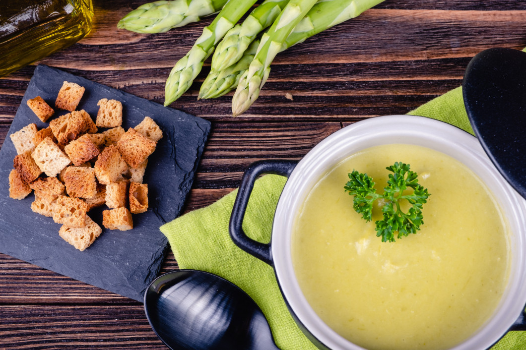 Fresh asparagus creamy soup and ingredients on a wooden table.