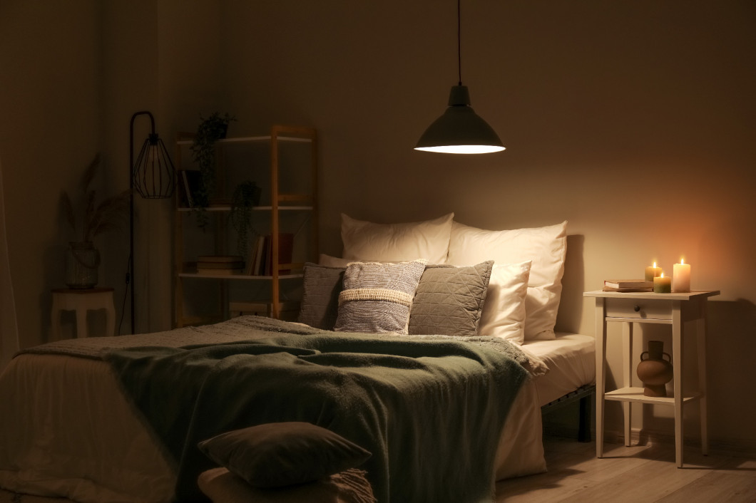 Interior of bedroom with green blankets on bed, burning candles and glowing lamp at night�