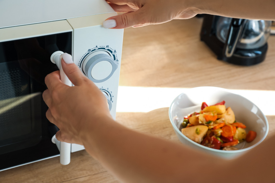 Woman opening modern microwave oven on wooden counter, closeup�