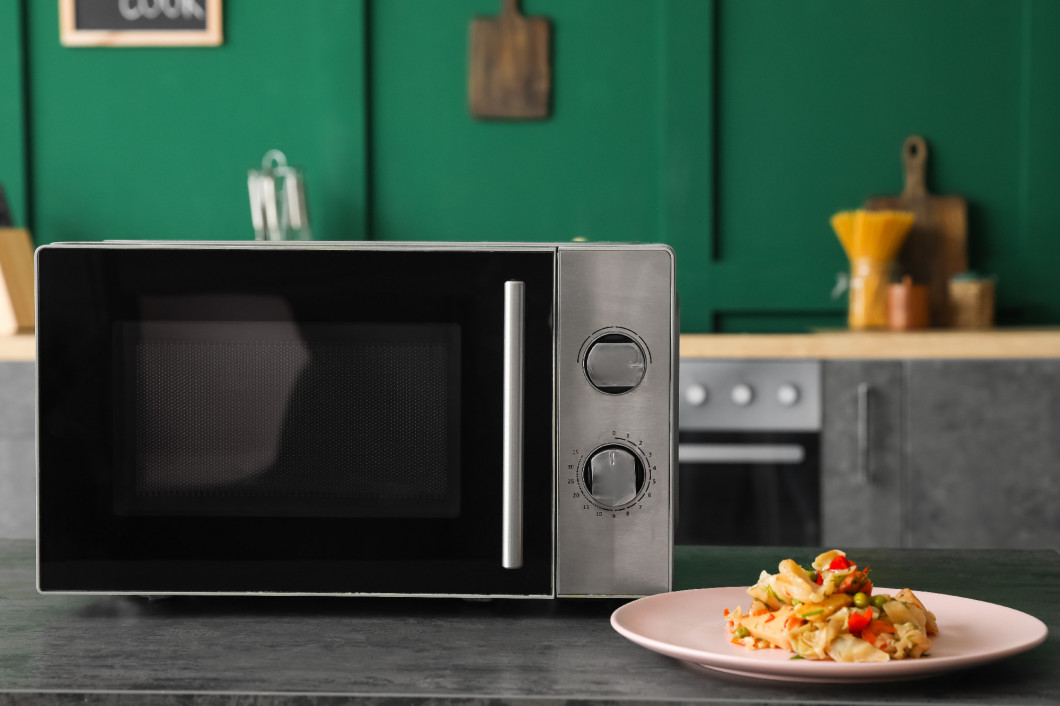 Modern microwave oven and plate with food on table in kitchen�