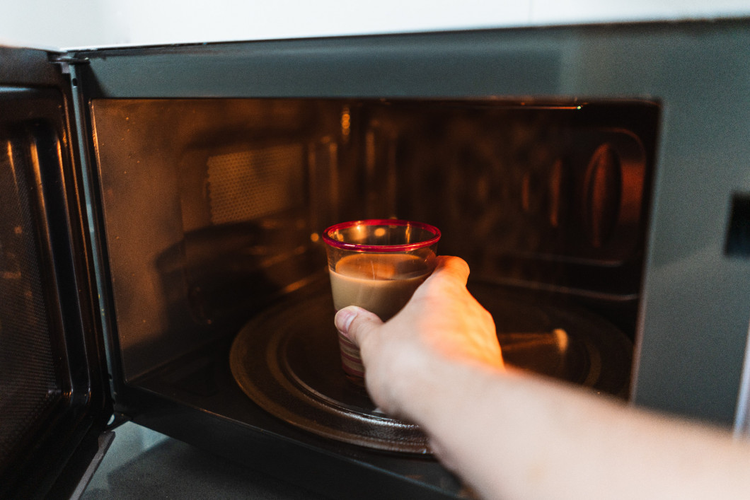 Closeup shot of a hand of the male putting a cup in the microwave to heat it