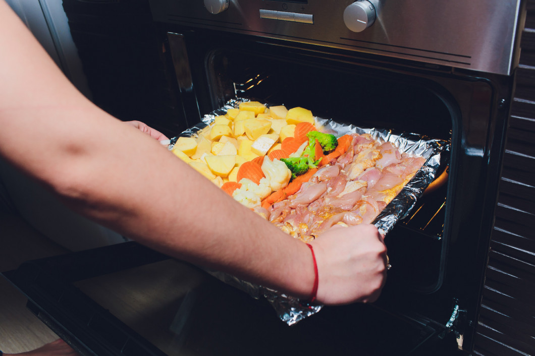 Cook taking ready fried baked chicken with vegetables from the oven. Home cooking concept.