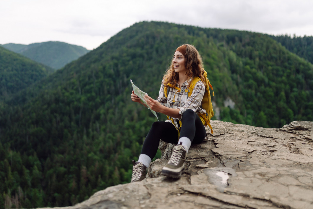 Traveler with yellow backpack and map in hands on a cliff in the mountains. Adventure concept.