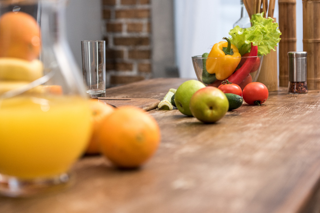 selective focus of orange juice in glass jug, fresh fruits and vegetables on kitchen table