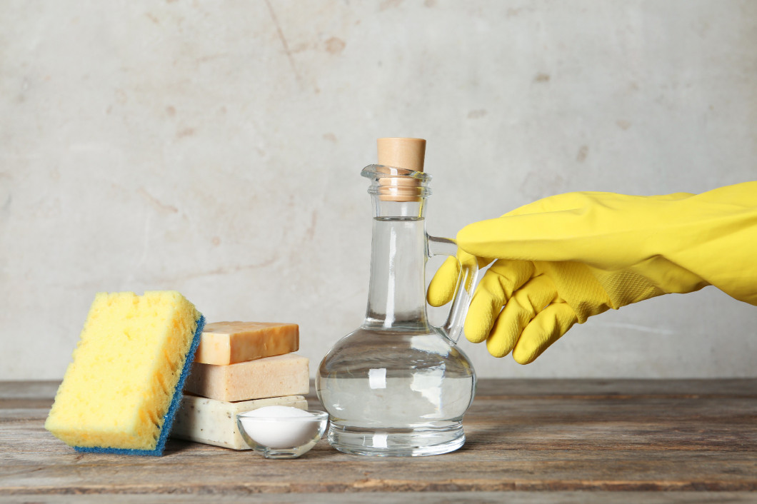 Woman with jug of vinegar and cleaning supplies at table�